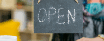 Shop owner holding a small chalkboard sign that says "Open"