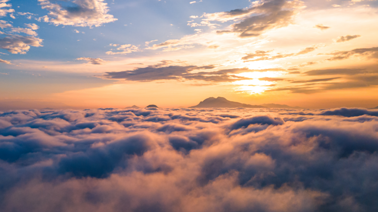 sunrise over the clouds with a mountain in the distance